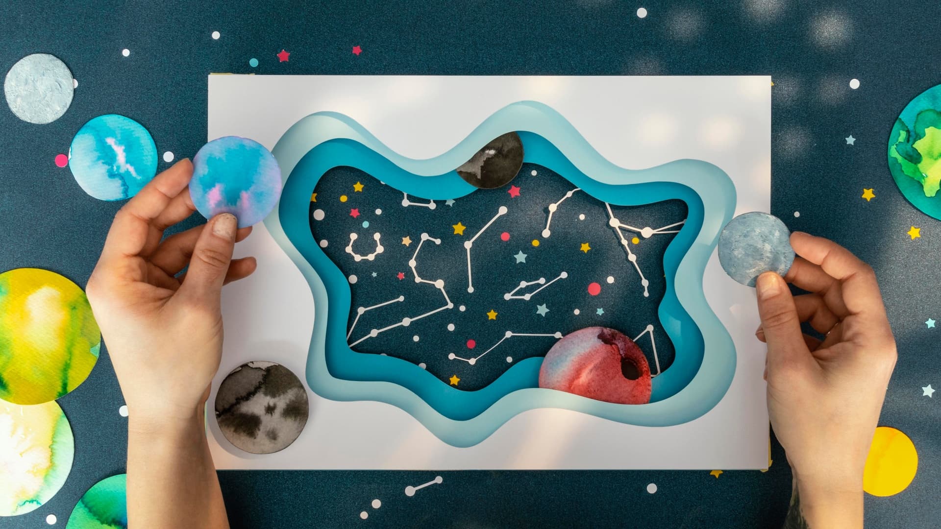 Hands holding a cosmic paper craft scene for astrology-based extracurricular activity ideas for kids